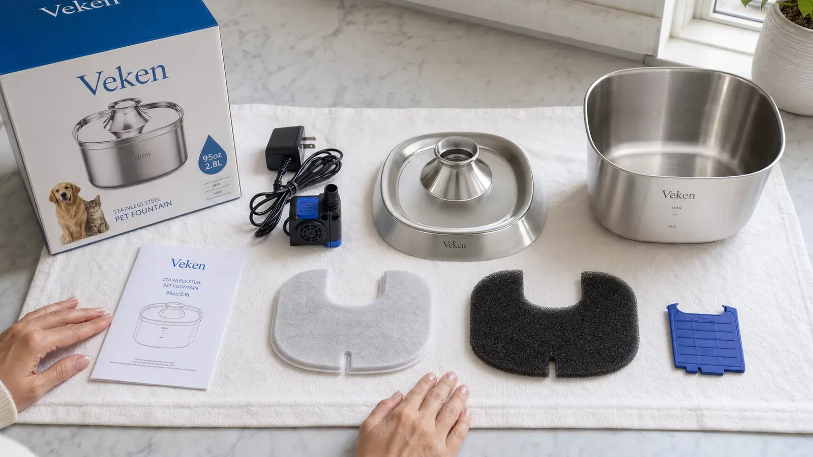 Disassembled Veken fountain parts laid out on a white towel showing filter, pump, and bowl components